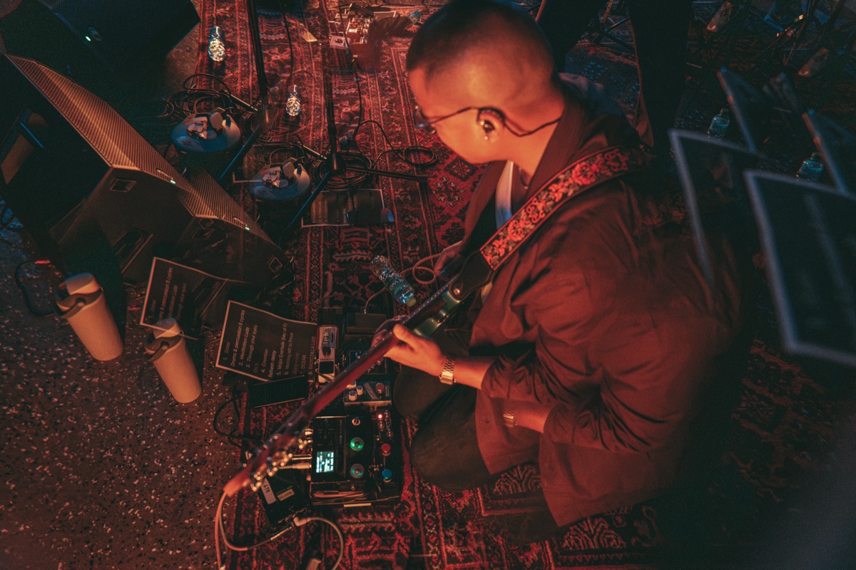 Overhead: the guitarist and pedalboard on a patterned rug